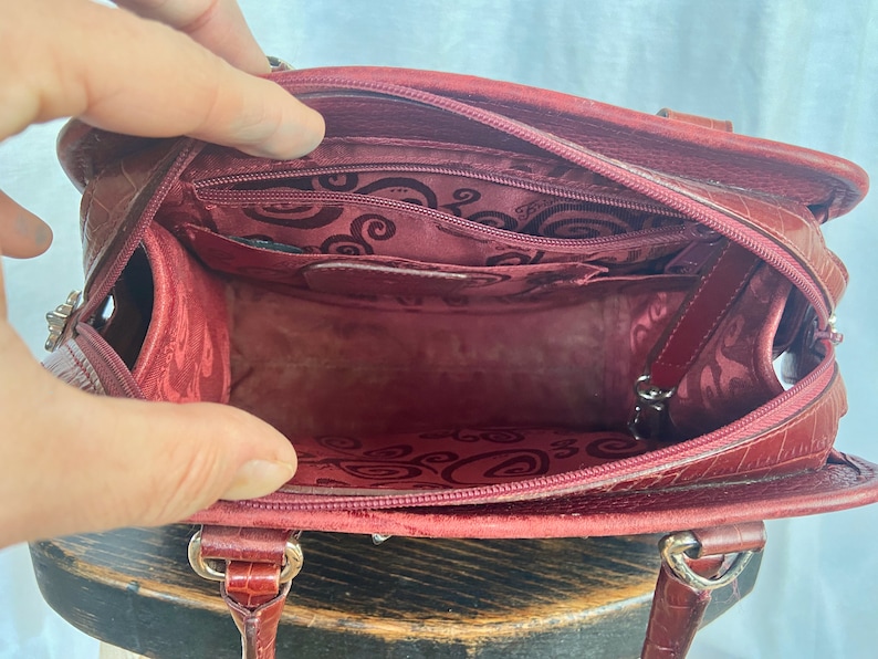 May include: A red leather handbag with a zipper closure and a patterned lining. The bag has a top handle and a shoulder strap.