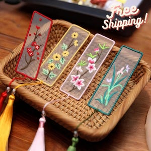 May include: Five colourful embroidered bookmarks with floral designs and tassels. The bookmarks are displayed in a wicker basket.