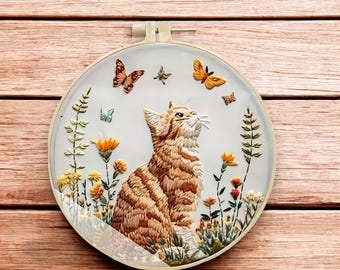 May include: Embroidered hoop art featuring a brown tabby cat sitting in a field of yellow, orange, and white flowers with butterflies flying above.
