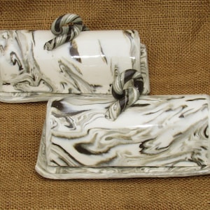 May include: Two ceramic butter dishes with swirl designs in black and white. Each dish has a unique, twisted handle.