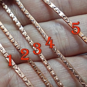 Könnte beinhalten: Fünf kupferfarbene Metallstäbe mit geätzten geometrischen Mustern. Jeder Stab hat ein einzigartiges Design, einschließlich Dreiecken, Punkten und Linien. Die Stäbe werden in einer Hand gehalten, um ihre komplizierten Details und ihre Handwerkskunst zu zeigen.