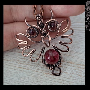 Op de afbeelding: DIY draadgewikkelde uil hanger voor beginners door Gemseeker Studio. Een uil hanger van koperdraad met rode edelsteen accenten.