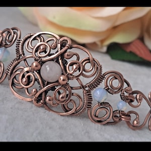 May include: A DIY copper wire bracelet with a delicate, intricate design featuring white opal and rose quartz gemstones. The bracelet is made by Gemseeker Studio, a company that specializes in creativity, imagination, and ideas.