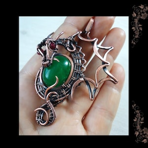 May include: DIY Wire Wrapped Dragon Pendant by Gemseeker Studio. A copper wire dragon pendant with a green gemstone and red accents.