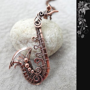 May include: A copper wire wrapped saxophone pendant, a DIY project by GemSeeker Studio. The pendant is on a white rock surface.