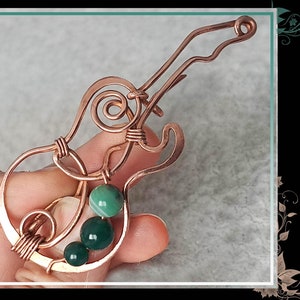 May include: DIY Guitar brooch for beginners by GemSeeker Studio. A copper wire guitar brooch with green gemstone accents.
