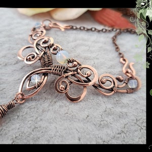 Puede incluir: Un collar de alambre de cobre envuelto con un diseño delicado e intrincado que presenta rizos y pequeñas piedras blancas. El collar tiene un colgante con una piedra rosa claro. El texto "DIY Wire wrap necklace with curls by Gemseeker Studio" es visible en la imagen.