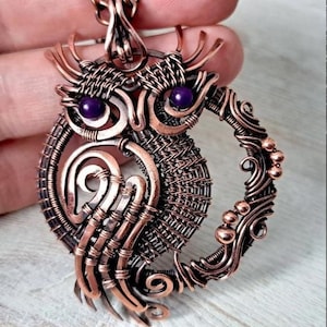 Może przedstawiać: DIY Wire Wrap OWL autorstwa Gemseeker Studio. Wisiorek w kształcie sowy z drutu miedzianego z fioletowymi oczami z kamieni szlachetnych.