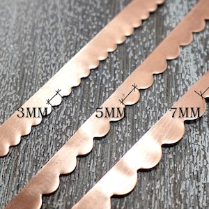 以下が含まれることがあります： スカラップエッジの銅色の金属ストリップが3本。ストリップには3mm、5mm、7mmの測定値が記載されています。それらは、テクスチャ加工された灰色の表面にあります。