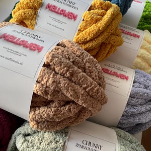 May include: A selection of vibrant chunky chenille yarn skeins in shades of yellow, blue, green, and beige. Each skein is labelled with the text "MELLOWEM" in pink, and "CHUNKY ŽENILKOVÁ PRIADZA". Ideal for knitting projects.