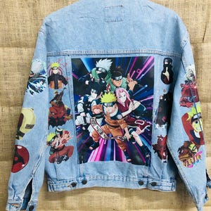 May include: A light blue denim jacket featuring a large printed image of characters from the anime series Naruto. The jacket has several smaller patches of Naruto characters on the sleeves and back.