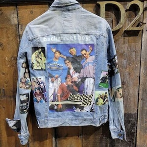 Könnte beinhalten: Eine blaue Jeansjacke mit einem Backstreet Boys-Patch auf der Rückseite. Der Patch zeigt eine Gruppe von fünf Männern in einer Band, mit den Worten "Backstreet Boys" darunter. Die Jacke hat mehrere Patches auf der Vorderseite und den Ärmeln, die Bilder der Bandmitglieder zeigen.