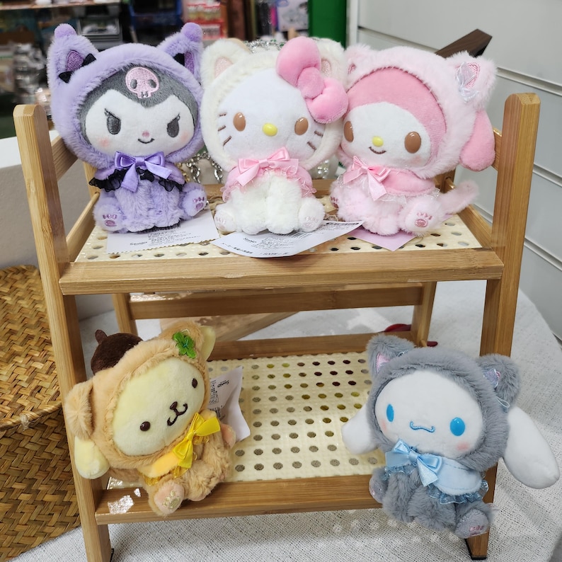 May include: Four plush toys on a wooden shelf. The toys are a purple and black cat, a white cat with a pink bow, a pink cat with a pink bow, and a brown and yellow dog.
