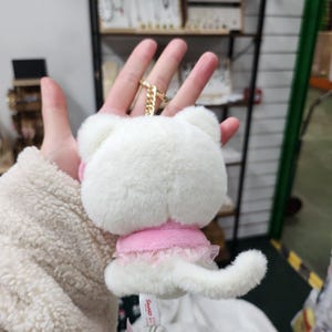 May include: White plush keychain with a pink dress and a white fluffy tail. The keychain is attached to a gold chain.