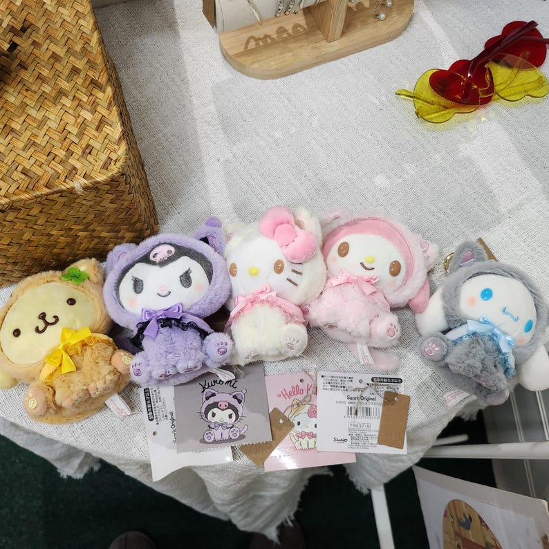 May include: Five plush toys, including a brown bear, a purple bat, a white Hello Kitty, a pink My Melody, and a gray cat. The toys are all wearing different outfits and have different expressions on their faces.