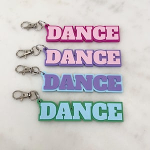 May include: Four keyrings with the word "DANCE" in a bold, blocky font. Each keyring is a different colour: pink, purple, blue, and green. Each keyring has a silver clasp.