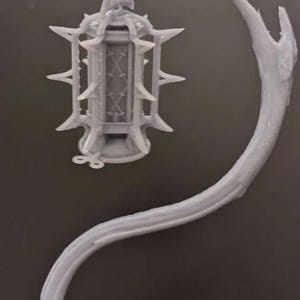 May include: A gray, ornate lantern with a spiky design, suspended from a curved, branch-like structure. The lantern features a detailed cage design and is likely a decorative item or a miniature model.