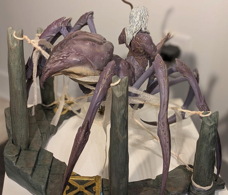 May include: A detailed fantasy sculpture of a large, purple spider with a rider. The spider has multiple legs and a textured body. The rider has long white hair and is wearing armor. The sculpture is set on a stone-like base with wooden posts.
