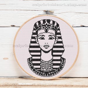 May include: A black and white cross-stitch design of an Egyptian pharaoh's face, presented in a wooden embroidery hoop. The pattern shows the pharaoh's headdress, face, and collar in detail. The Etsy shop name is visible at the top and bottom of the image.