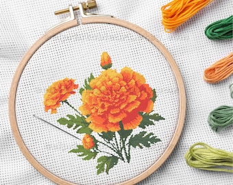 May include: A cross-stitch embroidery hoop with a bright orange marigold flower design and green leaves. The embroidery is set in a wooden hoop, with orange, green, and yellow embroidery threads in the background.