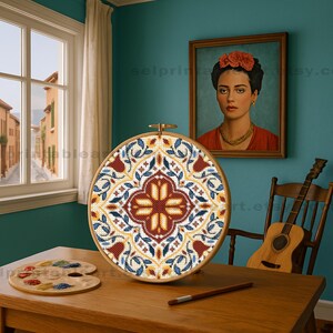 May include: A close-up of a completed embroidery hoop with a colorful geometric pattern. The hoop is on a wooden table with a paint palette and a pencil. A framed portrait of a woman with a flower crown hangs on the wall behind the hoop.