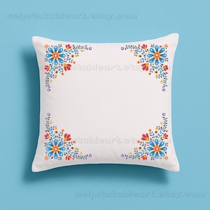 Può includere: Cuscino quadrato bianco con disegni floreali ricamati agli angoli. Il motivo floreale comprende fiori blu, rossi e gialli con foglie verdi. Il cuscino ha un aspetto strutturato ed è posto su uno sfondo azzurro.