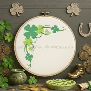Puede incluir: Un bastidor de bordado con un diseño de trébol de punto de cruz en verde y verde claro. La imagen incluye monedas de oro, una olla verde, una bota en miniatura y una tarta, todo con el tema del Día de San Patricio.