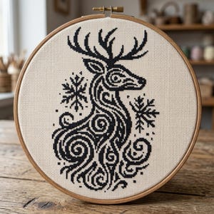 May include: A cross-stitch embroidery featuring a black deer design with antlers and snowflake accents. The artwork is set within a round wooden embroidery hoop, showcasing a detailed, symmetrical pattern on a cream-colored fabric. The design is suitable for home decor.