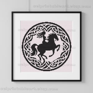 May include: Framed black and white cross-stitch art featuring a rider on horseback within an oval Celtic knot design. The artwork is set against a light pink background and framed in a black frame. The Etsy shop URL is visible at the top and bottom.