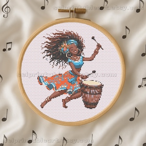 May include: Cross-stitch hoop art featuring a vibrant illustration of a woman playing a drum. She wears a blue top and an orange skirt with a floral pattern. The wooden hoop is set against a background with musical notes.