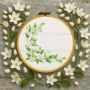 Puede incluir: Un bastidor de bordado de punto de cruz con un diseño floral de flores blancas y hojas verdes. El bastidor está rodeado de flores y capullos blancos sobre una superficie de madera azul claro desgastada. El texto "[email protected]" es visible.