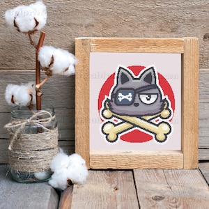 以下が含まれることがあります： 漫画の猫のデザインが施されたフレーム付きプリント。猫は、眼帯と交差した骨を持つグレーです。背景は赤い円です。フレームは明るい茶色の木材でできています。画像は木製の表面にあります。