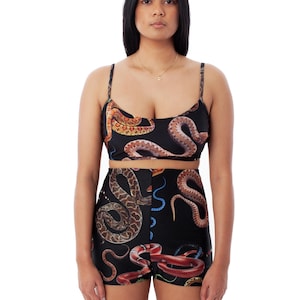 Puede incluir: Un traje de baño negro de dos piezas con estampado de serpiente. La parte superior es de estilo halter con tirantes finos y la parte inferior es un short de cintura alta.