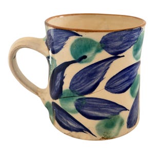 Puede incluir: Taza de cerámica color crema con asa curvada. Decorada con patrones de hojas azules y turquesas. El borde y el asa son de color marrón claro. Ideal para café o té.