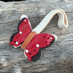 May include: A red and black leather butterfly keychain with white beads and a brown leather strap.