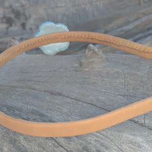 Puede incluir: Una diadema de ante marr&oacute;n con un detalle decorativo en el lateral.