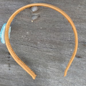 Puede incluir: Una diadema de cuero marr&oacute;n con un adorno de cuentas azules y blancas.