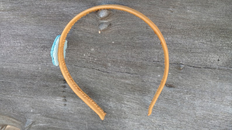Puede incluir: Una diadema de cuero marr&oacute;n con un adorno de cuentas azules y blancas.
