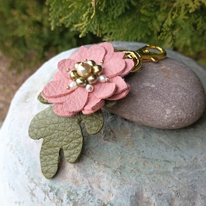 May include: A pink leather flower keychain with a gold metal clasp and white and gold beads in the center.