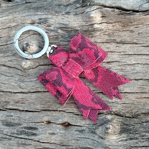 May include: A pink and black bow keychain with a silver metal ring.