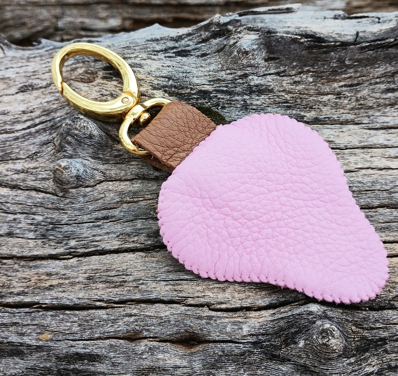 Puede incluir: Un llavero de cuero rosa con una correa de cuero marr&oacute;n y un anillo de metal dorado.