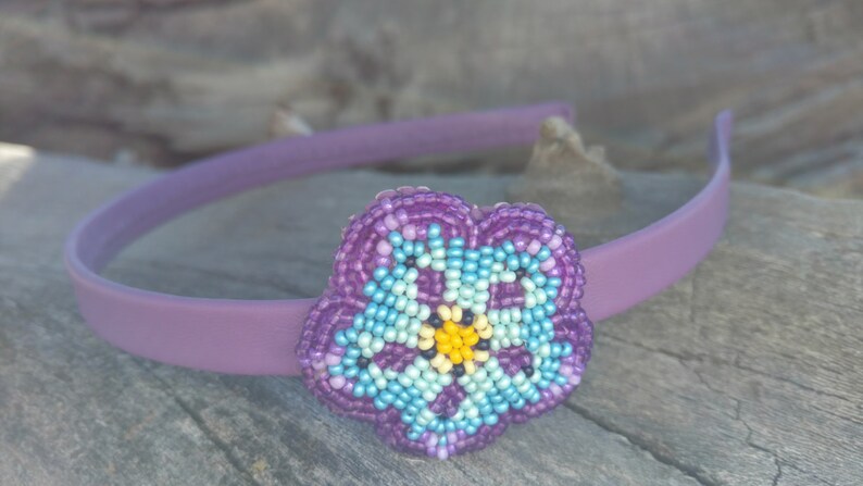 May include: Purple headband with a beaded flower accent. The flower is made of purple, blue, and yellow beads.