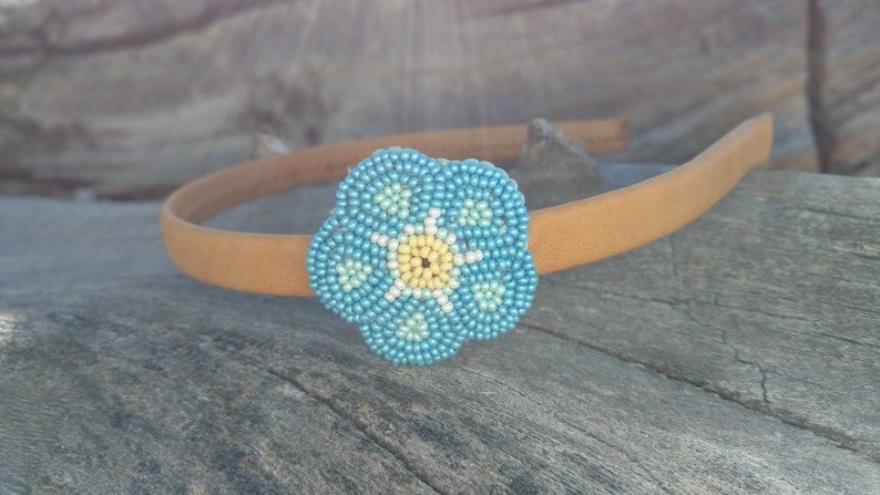 Puede incluir: Una diadema marr&oacute;n con un adorno de flor de cuentas azules y amarillas. La flor es un dise&ntilde;o de nomeolvides.