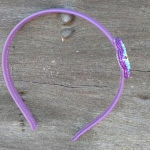 May include: A purple plastic headband with a beaded flower design in shades of purple, blue, and yellow.