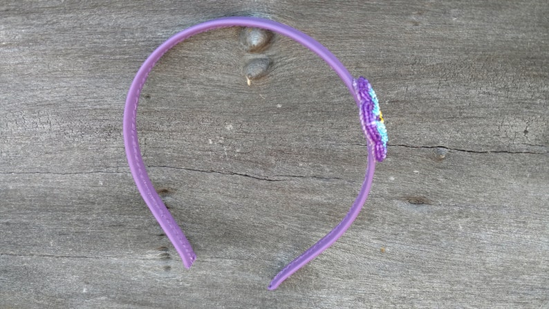 May include: A purple plastic headband with a beaded flower design in shades of purple, blue, and yellow.