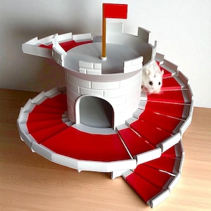 May include: A white and gray hamster castle with red carpeted spiral staircases. The castle has a cylindrical tower with a small arched doorway and a red flag on top. A small white hamster is visible.