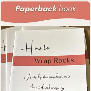 May include: An image featuring rocks adorned with woven and wrapped materials, and a paperback book titled "How to Wrap Rocks". The book's cover displays the title and the subtitle "A step-by-step introduction to the art of rock wrapping".