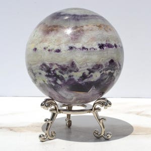 May include: A large, purple and white fluorite sphere on a silver stand. The sphere has a swirling pattern of purple and white.