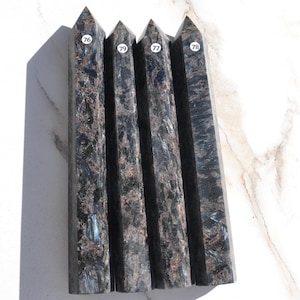 May include: Four tall, pointed stone towers with a dark, mottled texture in shades of black, brown, and metallic blue. Each tower is marked with a small white circular sticker featuring the numbers 76, 79, 77, and 78 respectively, arranged in a row.