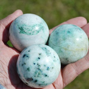 May include: Three smooth, polished green and white agate spheres. The spheres are about the size of a golf ball and have a mottled, swirling pattern.